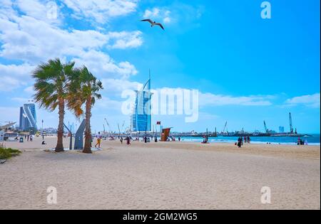 The sandy Public beach with lush palm trees and a view on Burj Al Arab and Jumeirah Beach luxury hotels, Dubai, UAE Stock Photo