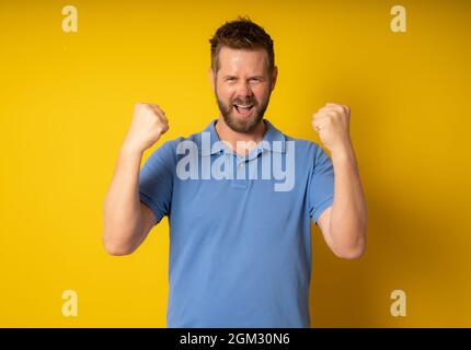 Young handsome man with beard wearing casual polo shirt standing over yellow background celebrating surprised and amazed for success with arms raised. Stock Photo