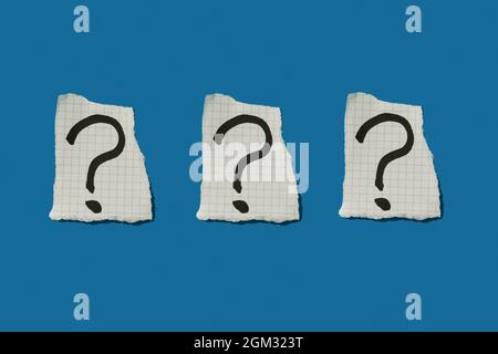 three question marks in three pieces of paper arranged in a line on a blue background Stock Photo