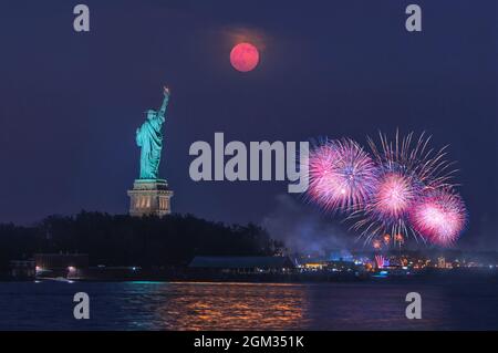 Statue Of Liberty Moon Rise - The super moon rises over the Statue of Liberty during the blue hour after sunset. In the background is a fireworks show Stock Photo