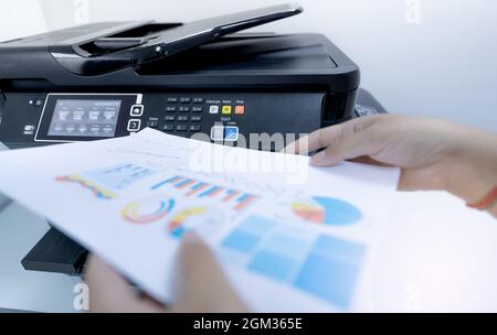 Office worker prints paper on multifunction laser printer. Copy, print, scan, and fax machine in office. Document and paper work. Print technology. Stock Photo