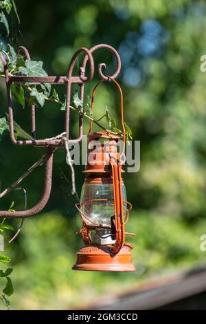 A single old red kerosene lantern hanging against a garden background in the yard in the ethnographic village of Holloko in Hungary Stock Photo