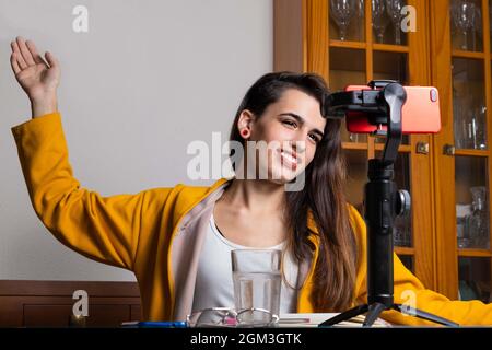 Happy female vlogger live streaming from living room using smartphoneHappy female vlogger live streaming from living room using smartphone Stock Photo