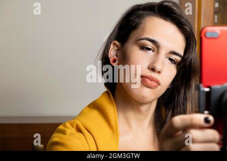 Happy female vlogger live streaming from living room using smartphone Stock Photo