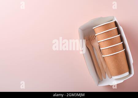 Paper cups, dishes, bag, wooden forks, drinking straws, fast food containers, wooden cutlery on pink background. Eco craft paper tableware. Recycling Stock Photo
