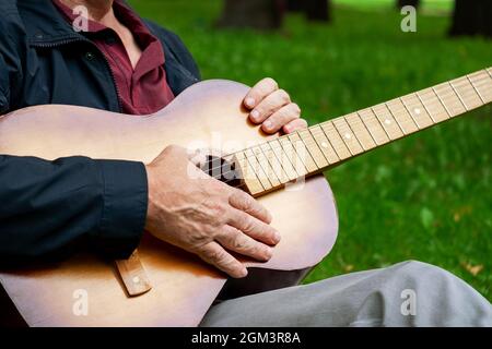 On a summer evening, an adult romantic man sits in a beautiful park on the grass and holds a six-string classical acoustic guitar in his hands. Select Stock Photo