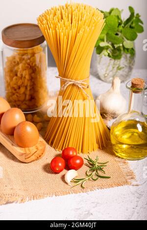 Carbo-diet  - spaghetti, ditalini raw pasta together with a jar of olive oil, cherri tomatoes, garlic and eggs in eco-wooden palette. Stock Photo