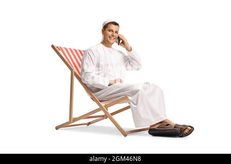 Young man in ethnic clothes itting on a beach chair and making a phone call isolated on white background Stock Photo