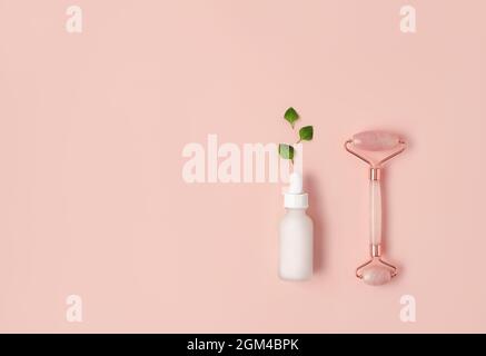 Beautiful composition of white mockup serum bottle, pink quarts stone face roller and fresh leaves on pink background. Natural cosmetics concept. Creative trendy cosmetics flat lay with copy space. Stock Photo