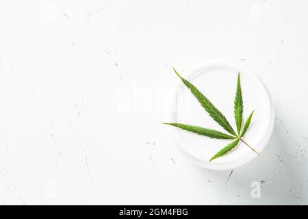 Cream jar with cannabis on white. Natural cosmetic. Stock Photo