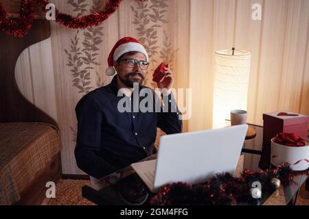 Virtual Christmas day house party. Man smiling wearing Santa hat Business video conferencing Online team meeting video conference calling from home. Stock Photo