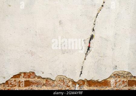 Rough plastered brick wall with cracks. Dirty damaged texture, peeling plaster, exposed brick on damaged wall. Vintage background, copy space Stock Photo