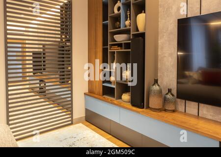 Modern living room interior with TV, open storage system, mirror panel with wood inserts on wall. Concept trendy interior in minimalist style, natural Stock Photo