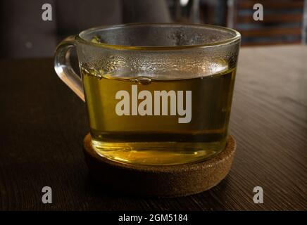 Transparent cup of green light tea on a cork stand on a brown table Stock Photo