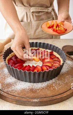 Woman cooking plum pie at table Stock Photo