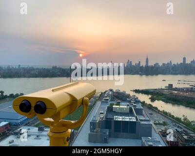 A binocular pointing the sunset behind Manhattan skyline from a rooftop in Williamsburg Stock Photo