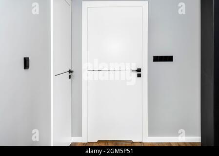A white door with a ventilation undercut with a matte black handle and a black line in the middle in a modern house with vinyl panels on the floor. Stock Photo