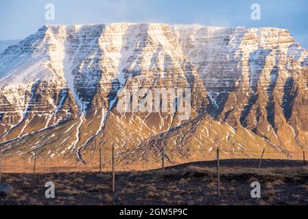 Golden hour lighting geological phenomenon in Iceland snow capped mountain wind blowing freezing texture layers landscape cliff edges wow Stock Photo