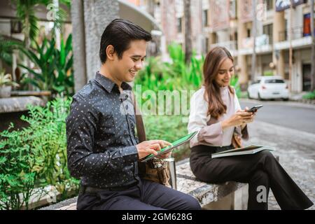 two busy worker sitting in the park during office break using phone Stock Photo