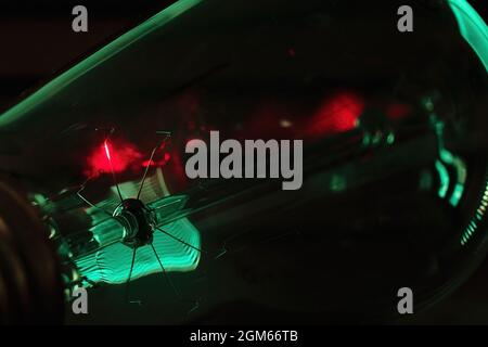 Lightbulb detail in macro view with glowing red filament and teal higlights on black background Stock Photo