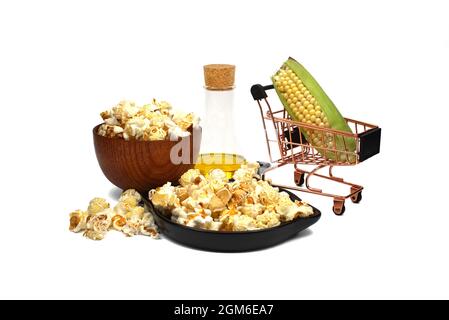 Fresh corn on the cob in a small shopping cart with bowls of popcorn snack spilling onto a white background with jar of olive, canola or sunflower oil Stock Photo