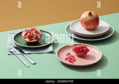 Close-up of pomegranate, half and seeds in pastel plate on green table with shadow on background. Minimali Stock Photo