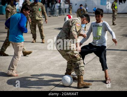 Soldiers assigned to the 1st Battalion, 6th Field Artillery Regiment, 41st Field Artillery Brigade play soccer with children from Afghanistan during Operation Allies Refuge at Ramstein Air Base, Germany, Sept. 10, 2021. Ramstein Air Base is a transit center that provides a safe place for the evacuees to complete their paperwork while security and background checks are conducted before they continue on to their final destination. (U.S. Army photo by Staff Sgt. Thomas Mort) Stock Photo