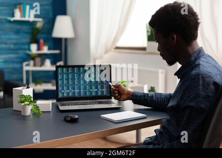 African american businessman doing market analysis working at cryptocurrency report analyzing blockchain chartsusing laptop in living room. Stock market exchange trading crypto currency on screen Stock Photo