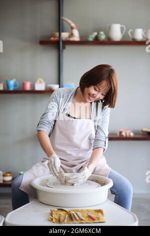 Happy pretty young smiling woman attending pottery class for beginners and making clay pot Stock Photo