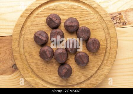 Several delicious chocolate truffles on a round wooden tray, close-up, on a wooden table, top view. Stock Photo