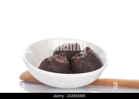 Three chocolate truffles in a white saucer with a wooden spoon, on a white plate. Stock Photo