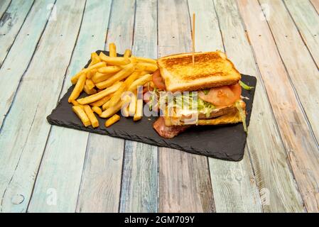 Great mixed sandwich with bacon, lots of melted cheese, fried egg, tomato and lettuce and a side of French fries Stock Photo