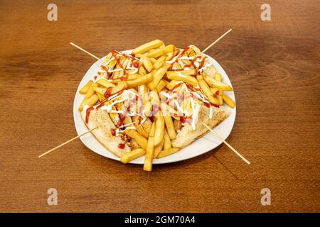 Club sandwich punctured with chopsticks in jumble with french fries on white plate Stock Photo