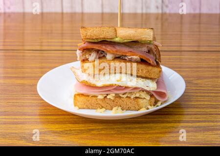 Super two-story sandwich with cheese, green sauce, fried bacon, shredded chicken, ham and fried egg with grilled sliced bread Stock Photo