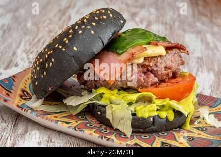 black bread burger with sesame seeds a good piece of minced beef, bacon, cheese and fried green peppers with lettuce and tomato Stock Photo