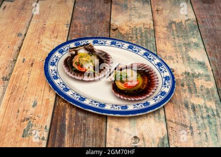 Dish decorated in blue tones with two wonderful Galician-style scallops with their cochas and Spanish olive oil Stock Photo