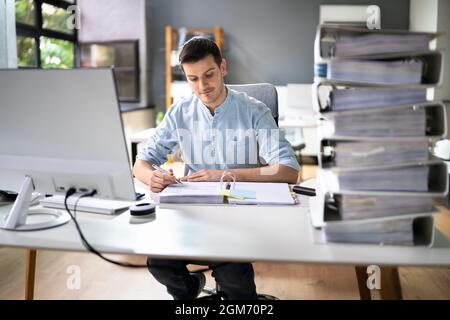 Young Businessman Working At Office With Stack Of Folders On Desk Stock Photo