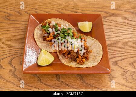 Two Mexican tacos with wheat tortillas stuffed with osso buco birria with pieces of lime to garnish on a clay plate Stock Photo