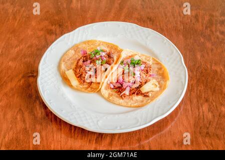 Two al pastor tacos with stewed meat, fried pineapple, red onion and chopped cilantro in corn tortillas on a white plate Stock Photo