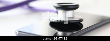 Medical instrument stethoscope lying on screen of mobile phone closeup Stock Photo