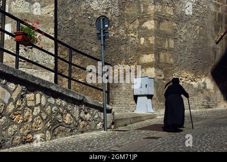 An elderly woman in a characteristic dress walks slowly through the streets of the village. Scanno, Abruzzo, Italy. Stock Photo