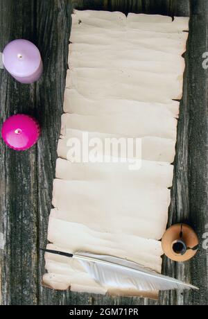 scroll of paper with place for text pen for writing and inkwell on a rough wooden table in the light of burning candles Stock Photo