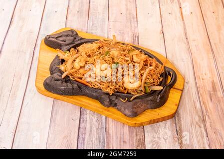 curly noodles sauteed with vegetables, white onions and peeled shrimp with soy sauce and a boiling cast iron griddle Stock Photo