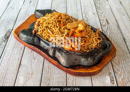 Mixed Chinese curly noodles with sauteed vegetables, with meat and with prawns on fiery cast iron plate Stock Photo