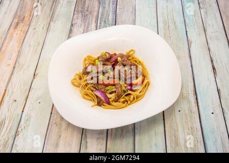 Peruvian-style sautéed noodles with striploin meat, fresh vegetables and red onion with soy sauce Stock Photo