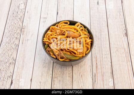 bowl of sauteed noodles with mushrooms, boletus and vegetables, peppers and onions with soy sauce on wooden table Stock Photo