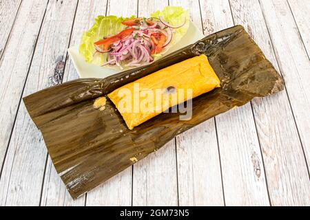 Mexican tamale stuffed with meat garnished with raw purple onion, strips of peppers and banana leaf Stock Photo