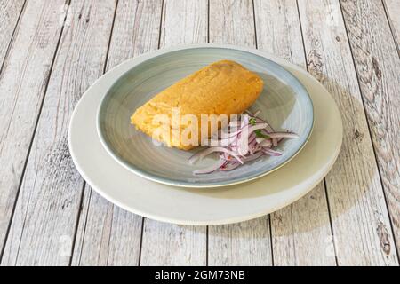 Mexican corn tamale stuffed with chicken meat stew with purple onion on blue plate Stock Photo