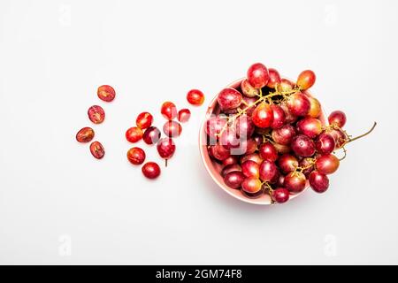 Clusters of claret color dessert grapes in pink bowl on white table Stock Photo
