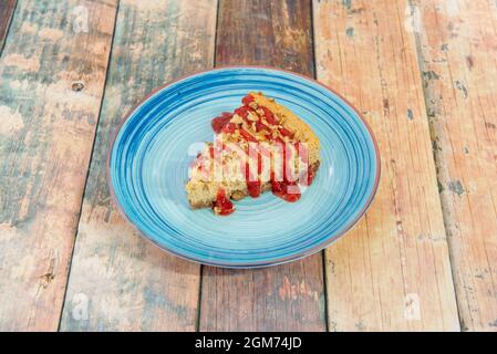 Portion of creamy cheesecake with strawberry jam and pieces of nuts on blue plate Stock Photo